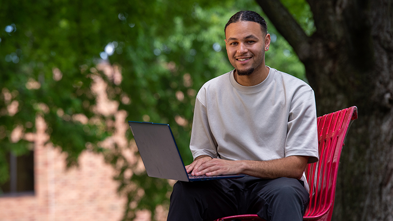 SCSU student seated on red bench working on laptop