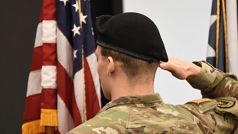 Military student saluting flag at Veterans Day event on campus