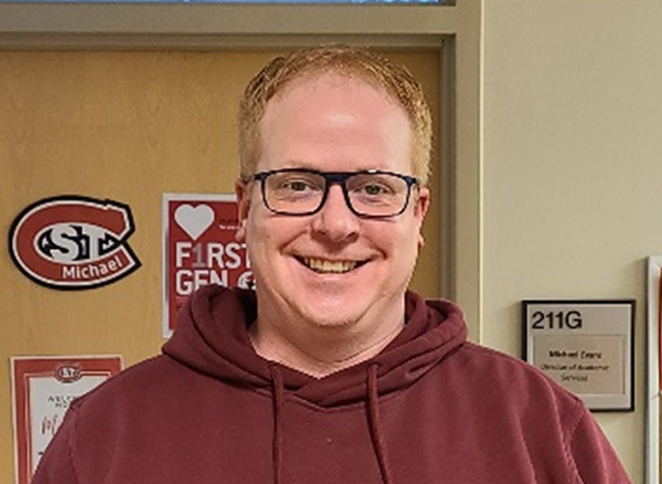 Brent Hanratty posing in front of a door with a St. Cloud State University logo  in the background