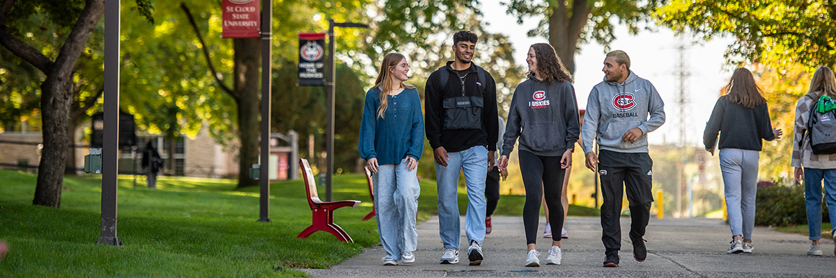 Four students walking and talking on campus sidewalk
