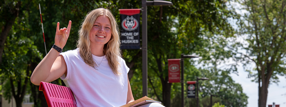 SCSU student on red bench giving "sign of the husky" with hand
