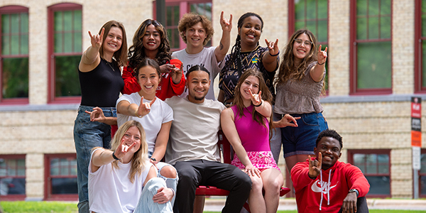 Group of SCSU students posed for photo doing the "sign of the husky" with hands