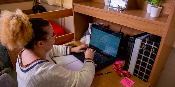 A student works on their laptop inside their SCSU dorm room