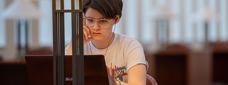 A student works on a laptop in the SCSU library wearing ear buds