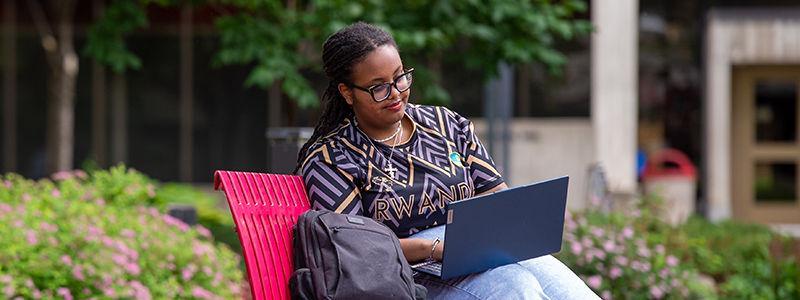 A student sits on a campus bench with laptop