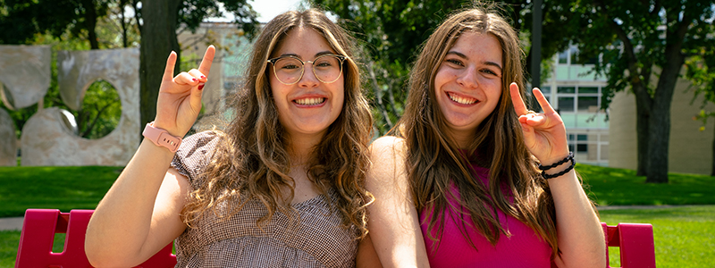 Two students smile and give the "sign of the Husky" with their hands