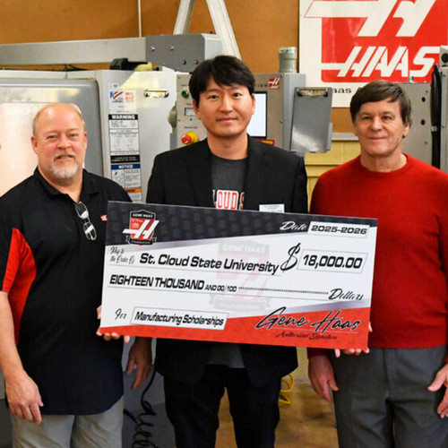 A group of three men hold a large check from the Gene Haas Foundation with Haas machinery visible in the background