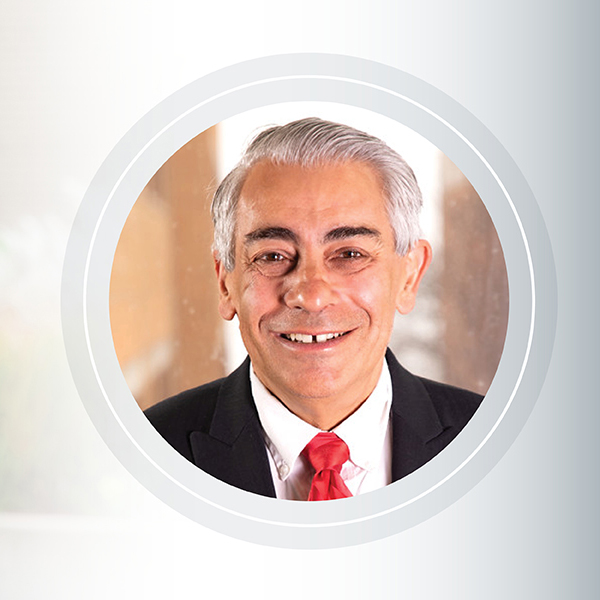 King Banaian, a man with grey hair, a black suit, red shirt and white tie smiles at the camera for a headshot