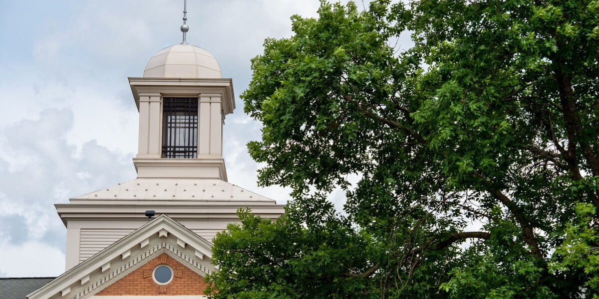 The white cupola of Lawrence Hall stands against a cloudy sky and green tree branches