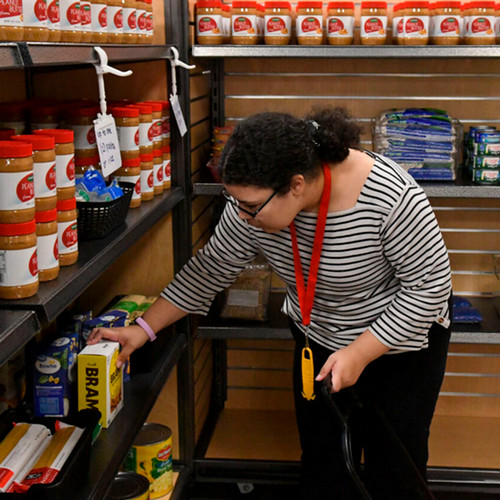 A woman with black hair and glasses looks at a box of food while standing in an aisle