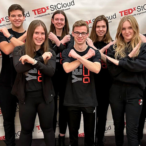 Six students have their arms crossed in an x while participating in TEDXStCloud