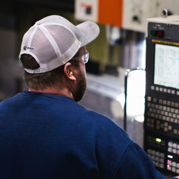 A man in a blue shirt and baseball cap turns a dial on a machine